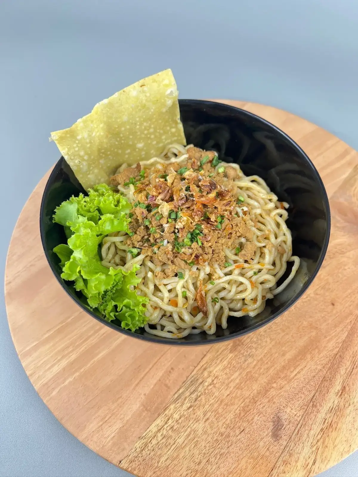 Mangkuk mie ayam dengan topping ayam, daun bawang, dan kerupuk pangsit